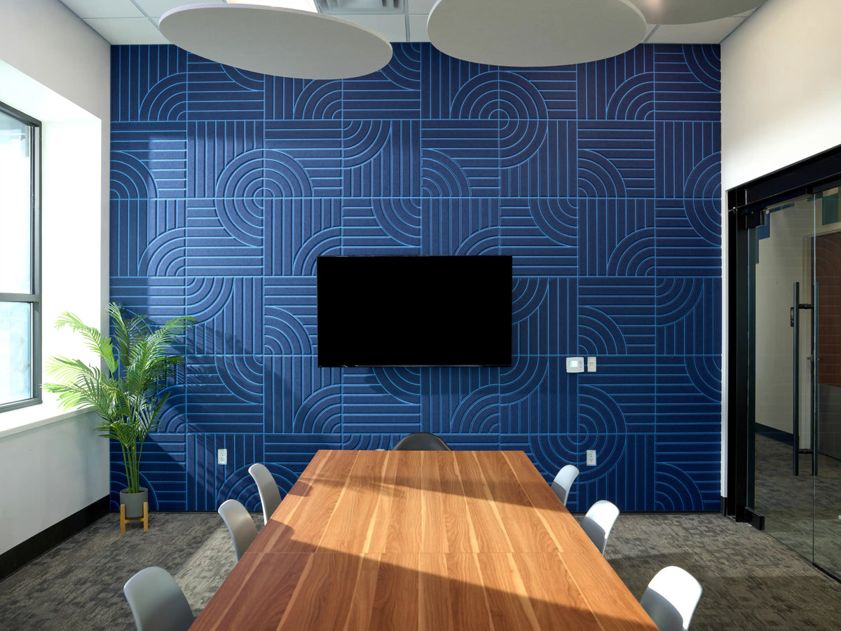 A modern conference room featuring a prominent blue geometric patterned accent wall with a mounted flat-screen TV, a long wooden table, and white chairs.