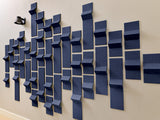 Three-dimensional navy blue tiles with varying depths and angles arranged in a geometric wall pattern on a beige surface.