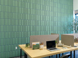 Green textured wall tiles with layered pattern behind office desk with laptop and supplies.