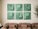 Six sage green tiles with dimensional geometric cutouts and folds arranged in a 2x3 grid on a wall above a brown sofa.