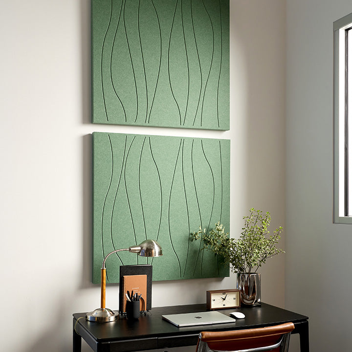 Two green acoustic felt wall panels with engraved wavy line patterns, displayed on a wall above a black desk in a modern home office setting.