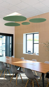 Green oval acoustic baffles suspended from ceiling in modern conference room above wooden table.