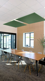 Two green square acoustic baffles suspended from ceiling above conference table in office space.