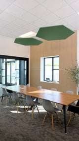 Two green hexagonal acoustic baffles suspended from ceiling above conference table in modern office space.