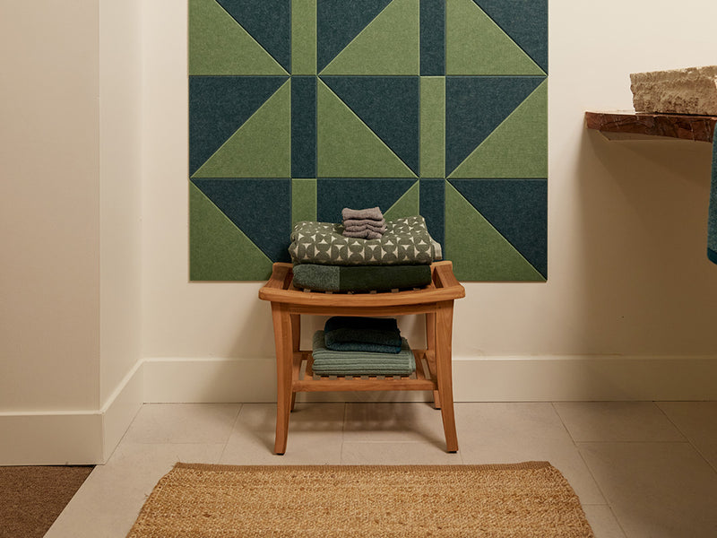 Felt Right wall art in shades of green felt tiles on a wall with a stool holding towels in a bathroom