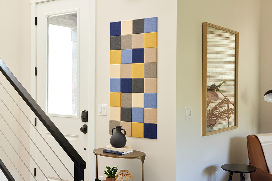 A Felt Right wall art design using squares to form a pattern in shades of blue, cream, grey, and yellow next to a door above a table.