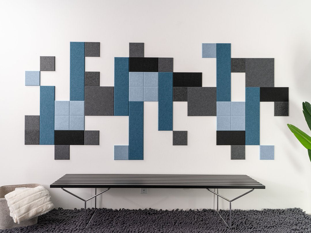 Felt Right wall art design with shades of grey and blue creating a geometric pattern on a white wall by a bench.