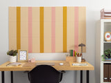 Peach, gold, and cream pinstriped cork bulletin board mounted on wall above wooden desk.