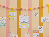 Bulletin board with peach, gold, and cream vertical pinstripes displaying children's artwork, educational charts, and a pom-p