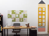 Wall-mounted pinboard with alternating green and beige fabric squares holding papers and notes above a wooden desk.
