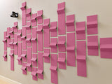 Pink three-dimensional tiles arranged in a wave pattern on a beige wall with a black speaker visible.