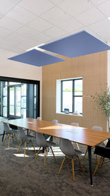 Two blue square acoustic baffles suspended from ceiling above conference table in modern office space.