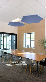Two blue hexagon-shaped acoustic baffles suspended from ceiling above conference table in office space.