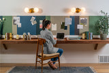 A Felt Right wall art design in shades of blues, greens, and browns felt that is pinnable and goes a long a desk with a woman working on a laptop.