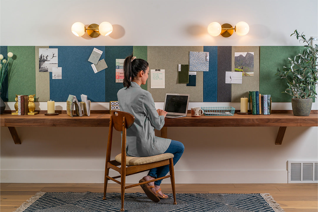 A Felt Right wall art design in shades of blues, greens, and browns felt that is pinnable and goes a long a desk with a woman working on a laptop.