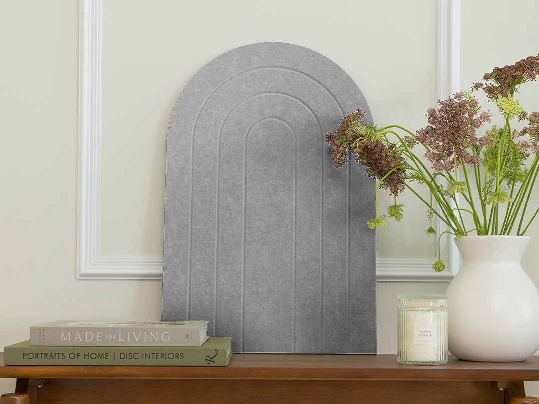 Decorative wall art with arches on a wooden table with books and a vase.