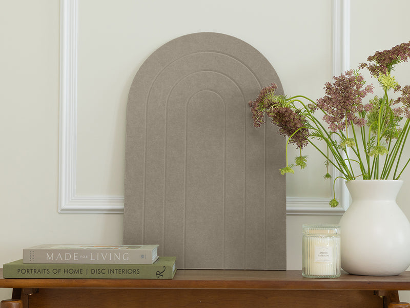 Decorative wall mirror with books and a vase on a wooden surface against a light-colored wall.