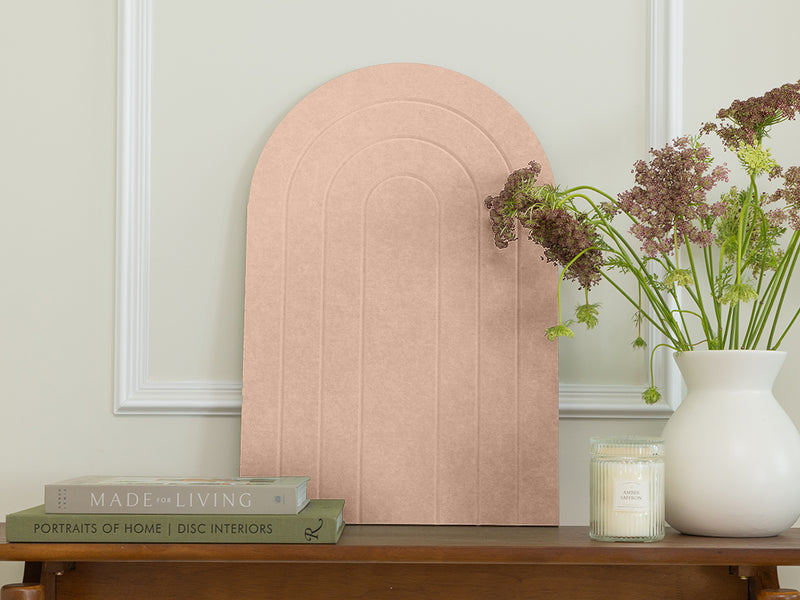 Pink arch-shaped headboard on a wooden table with books and a vase of flowers.