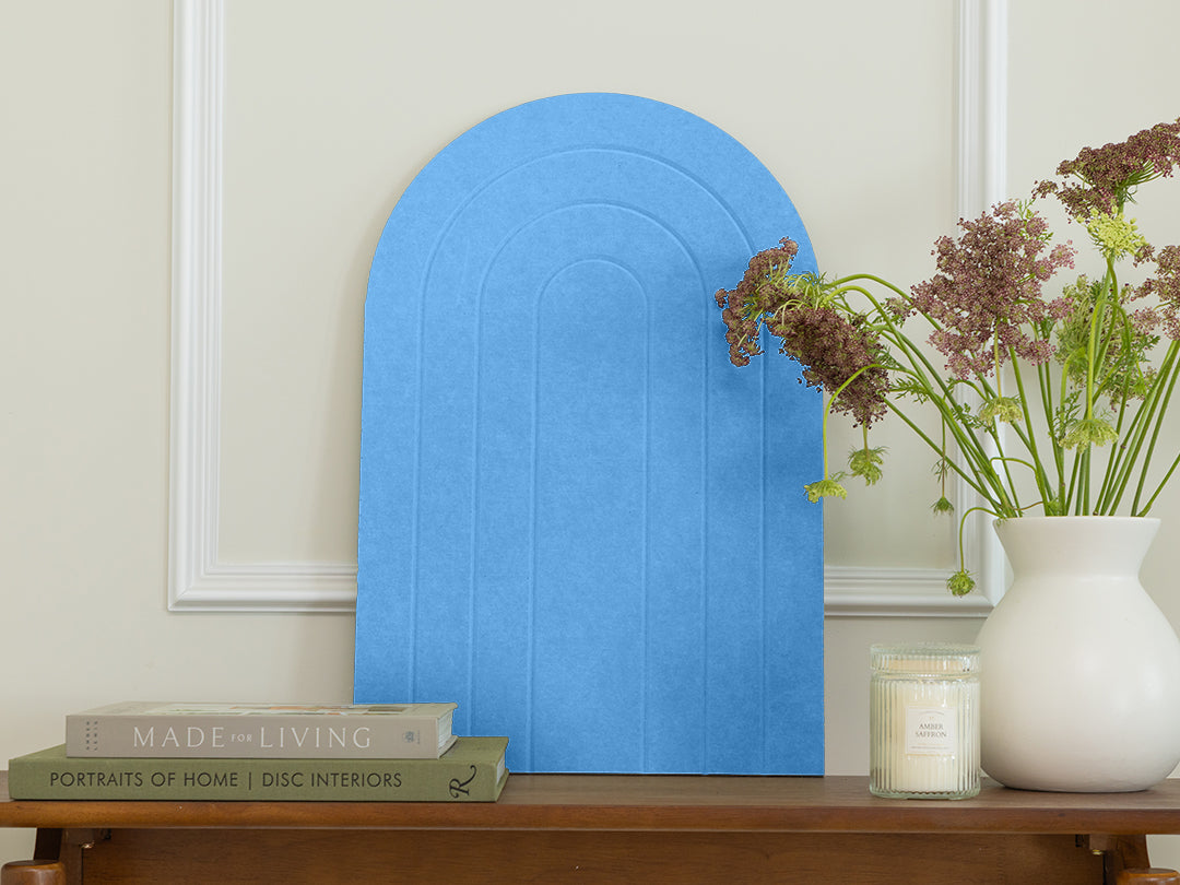 Blue arch-shaped wall art piece on a wooden shelf with books and a vase.