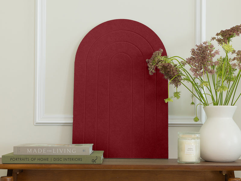 Red decorative wall panel on a neutral wall with books and a vase.