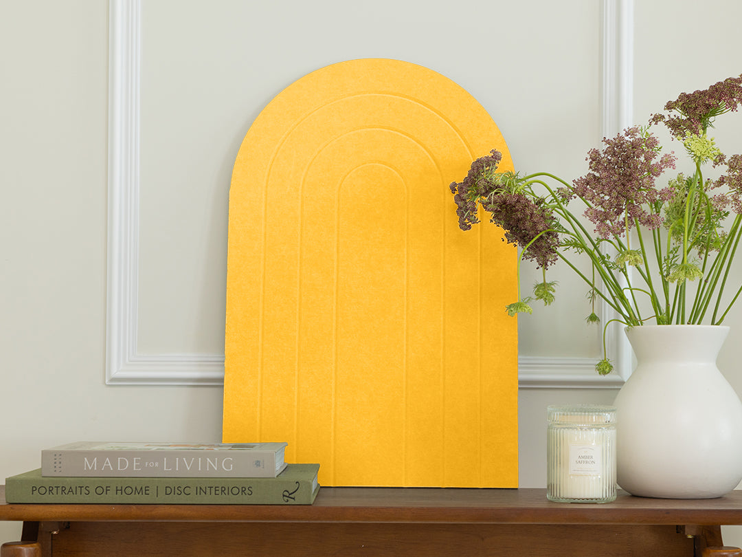 Yellow arch-shaped object on a wooden table with books and a vase in a room.
