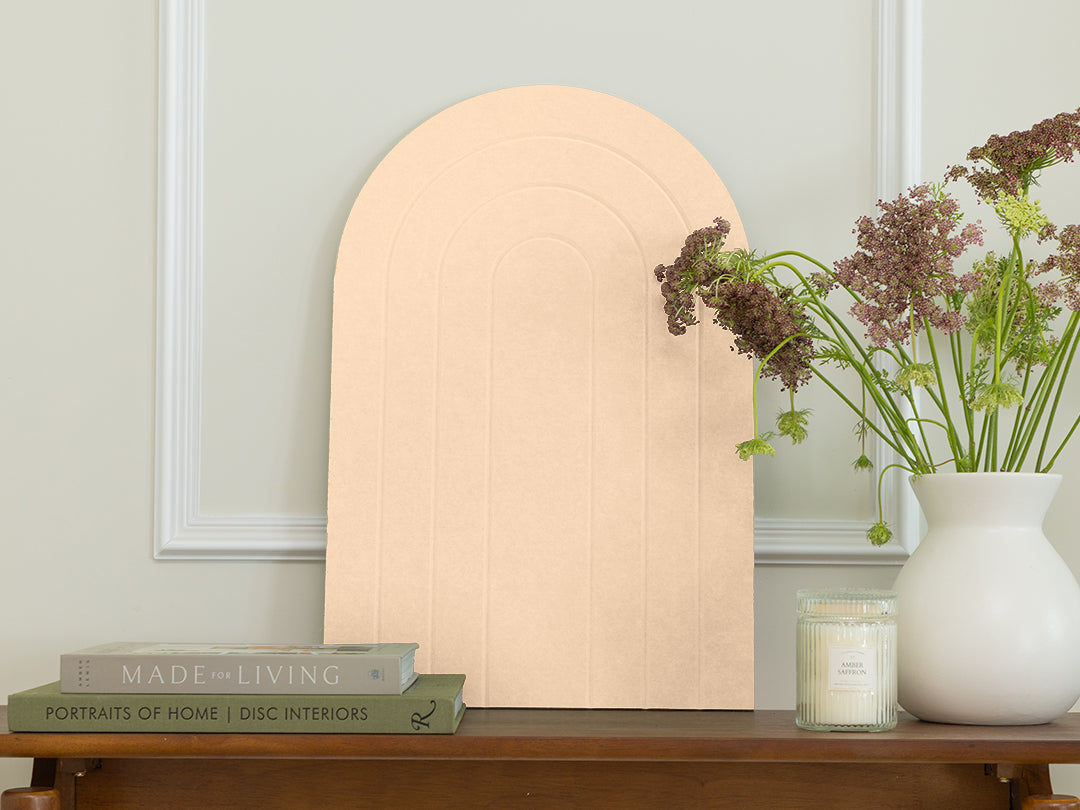 Wooden shelf with a decorative mirror, books, and a vase with flowers against a light gray wall.