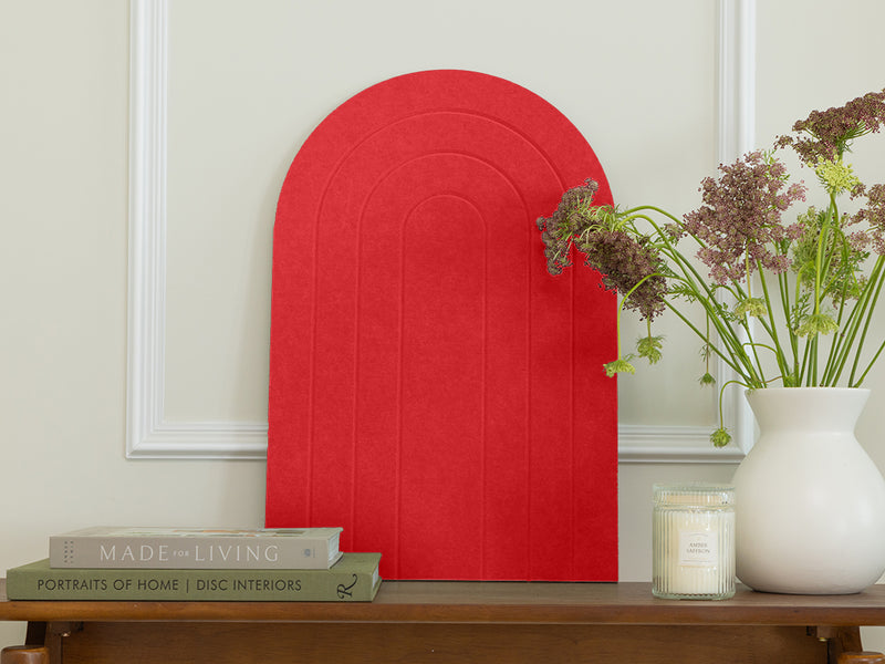 Red arch-shaped object on a wooden table with books and a vase of flowers.