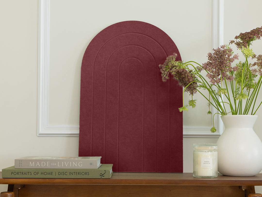 Decorative red archway on a wooden table with books, a candle, and a vase of flowers.