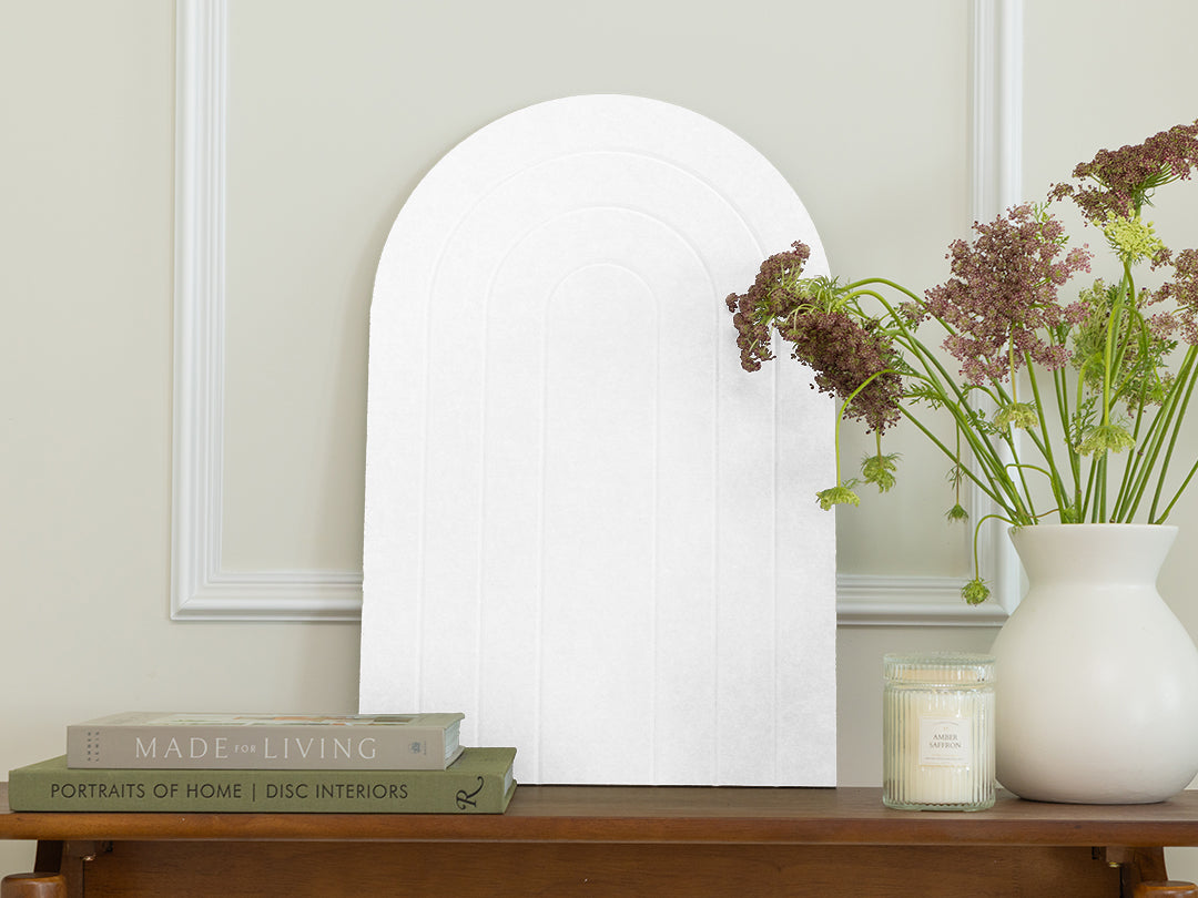 White oval mirror on a wooden table with books and a vase of flowers.