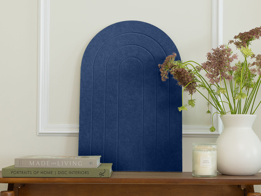 Navy blue wall art piece on a wooden shelf with books and a vase.