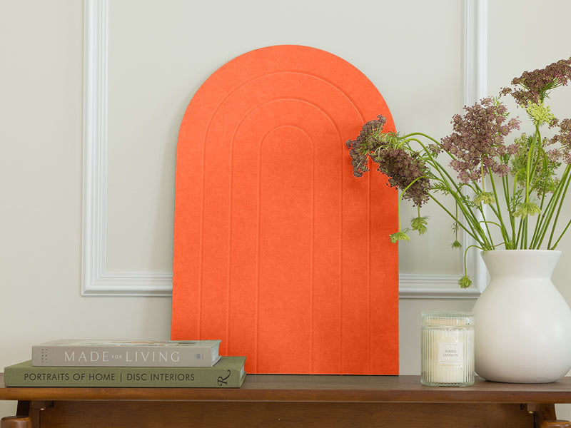 Orange arch-shaped wall art piece on a neutral wall with books and a vase on a table.