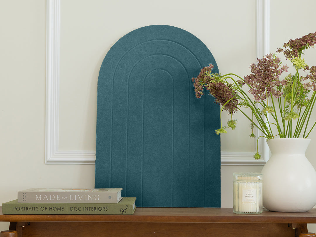 Teal arch-shaped mirror on a wooden table with books and a vase of flowers.