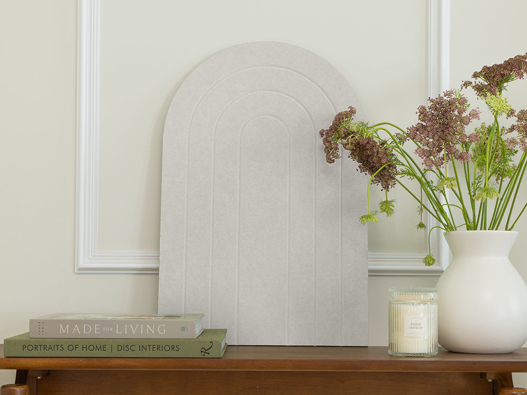 Decorative setup with a mirror, books, and a vase with flowers on a wooden surface.