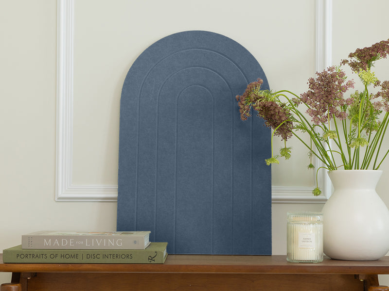 Decorative blue wall art piece on a wooden shelf with books and a vase.