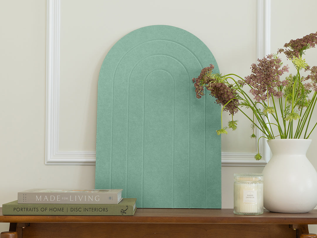 Decorative green wall art piece on a wooden table with books and a vase.