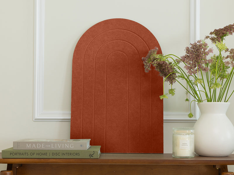 Decorative arch on a wall with books, a candle, and a vase with flowers on a table below.