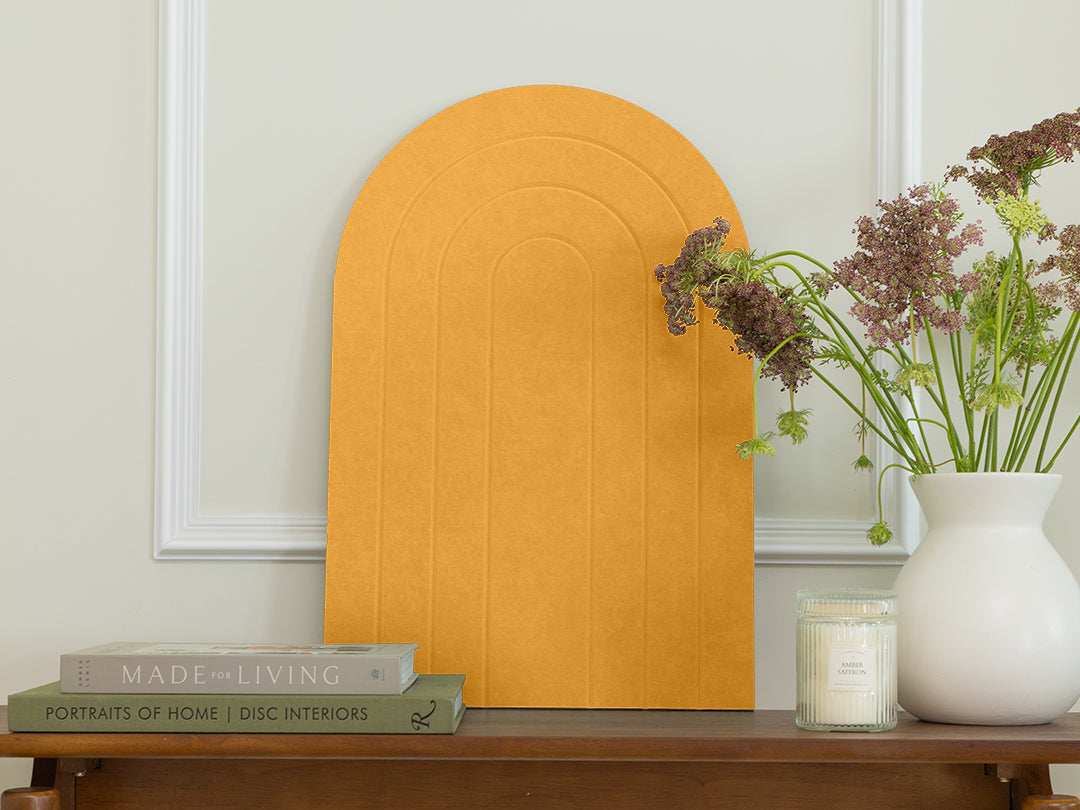 Mustard yellow arch-shaped mirror on a wooden table with books and a vase.