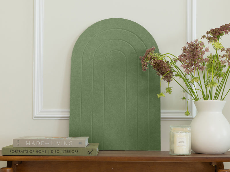 Decorative green wall art piece on a wooden table with books and a vase.