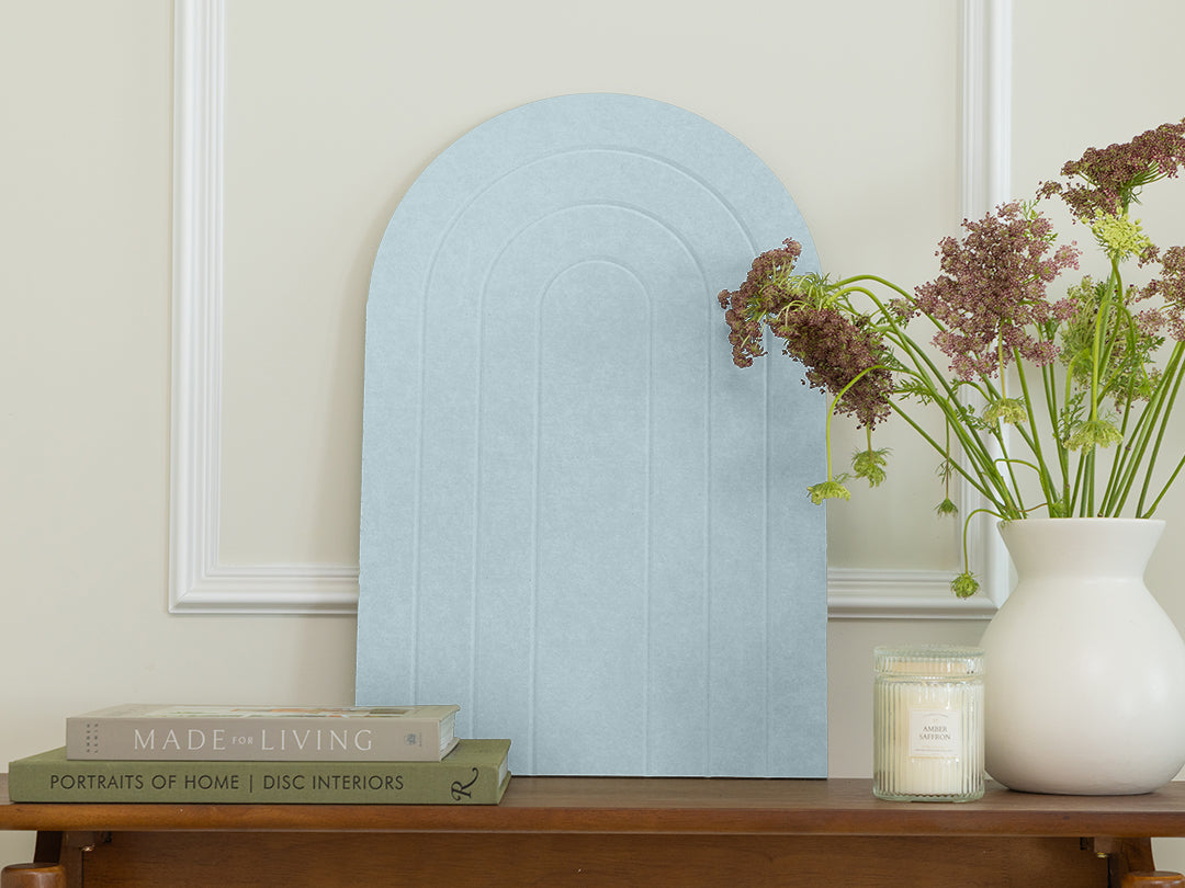 Light blue arch-shaped mirror on a wooden surface with books and a vase in the background.