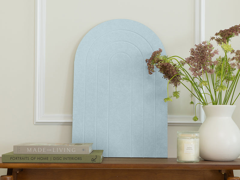 Light blue arch-shaped mirror on a wooden surface with books and a vase in the background.