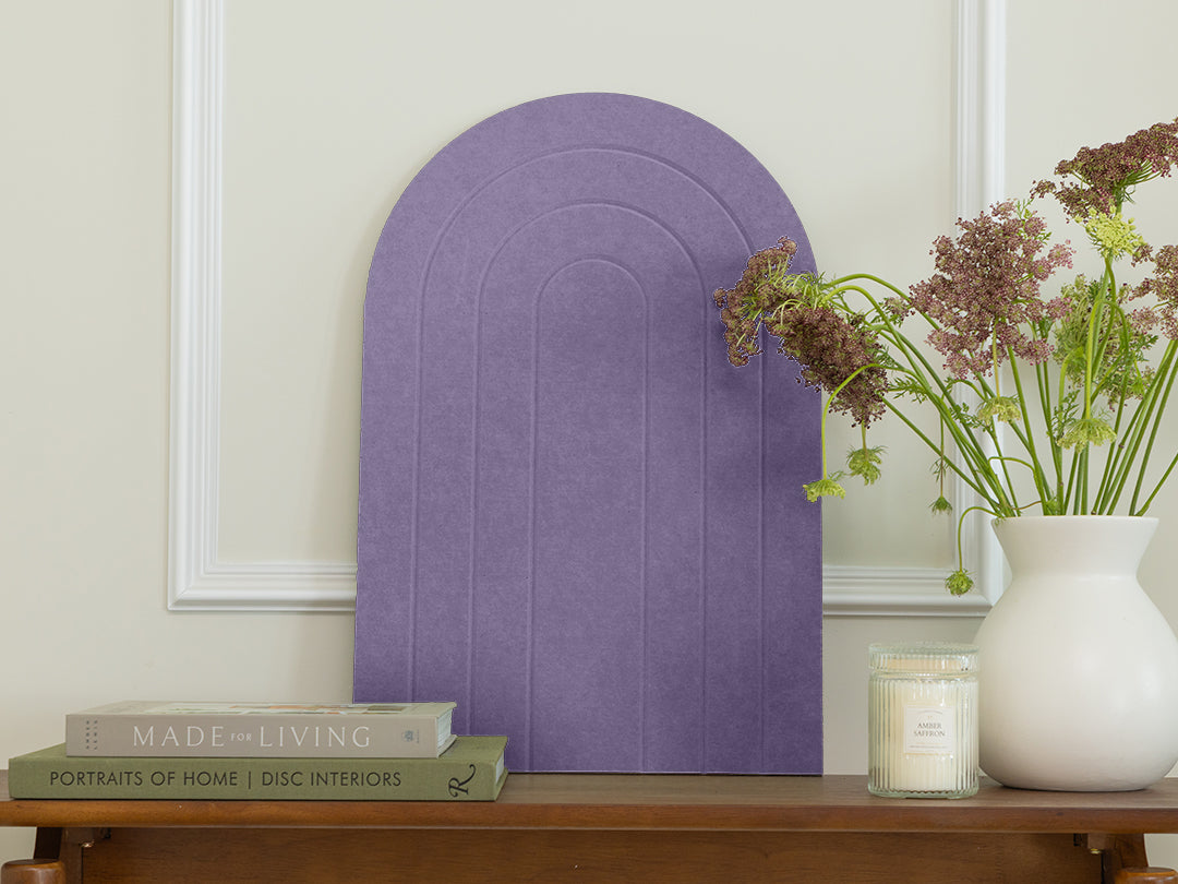 Purple arch-shaped wall art on a neutral wall with books and a vase of flowers on a wooden surface.