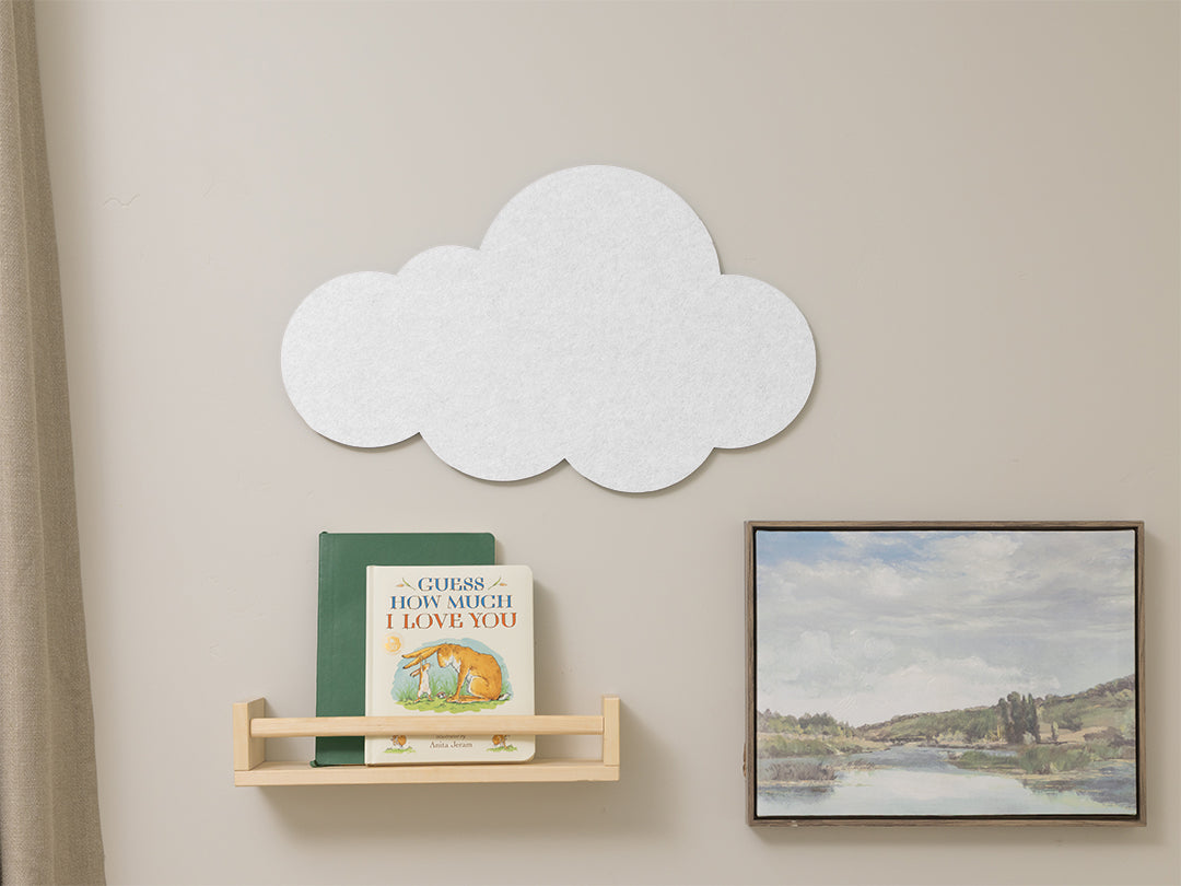 White cloud-shaped wall decoration on a beige wall with books and a painting.