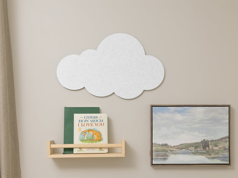 White cloud-shaped wall decoration on a beige wall with books and a painting.