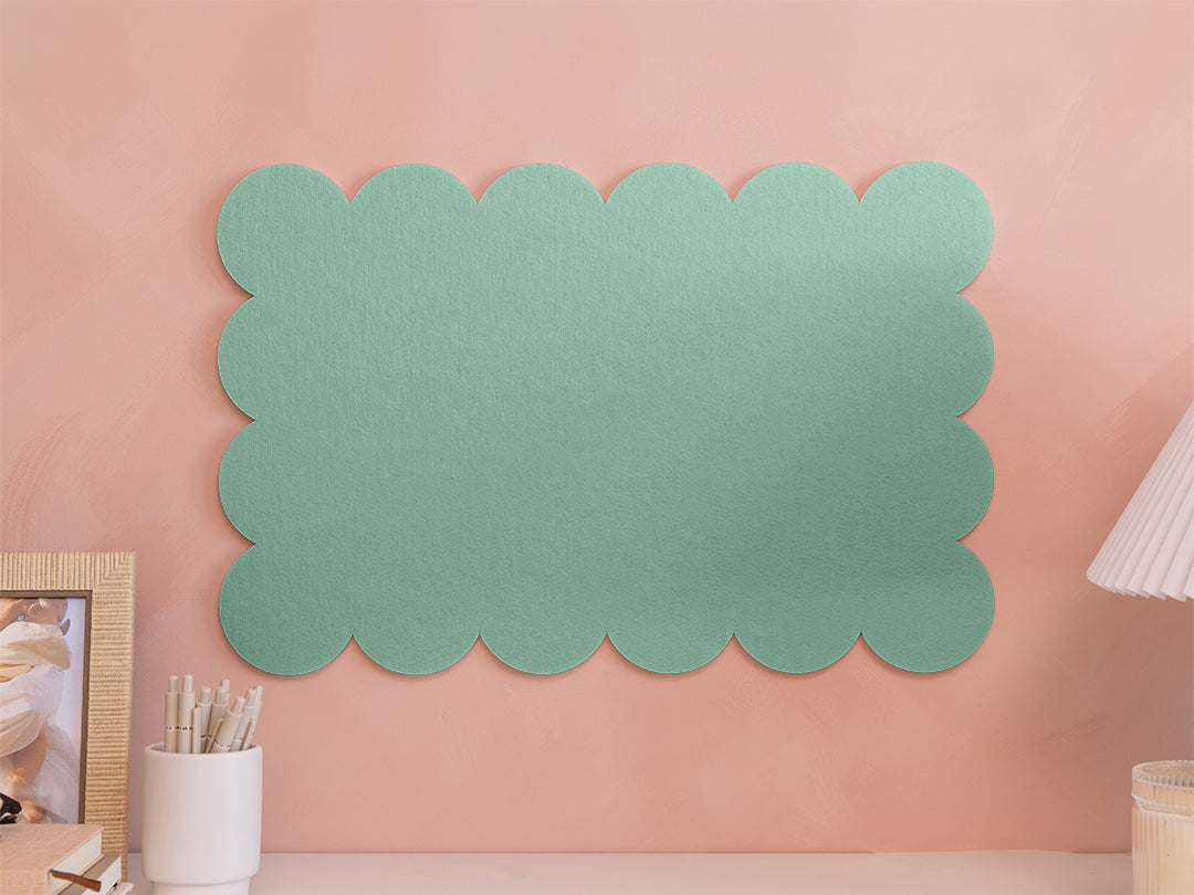 Green scalloped wall art on a pink wall with decor items.