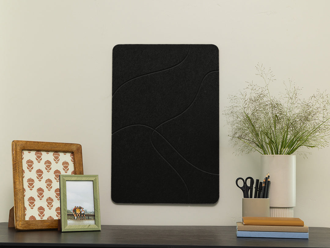 Black decorative wall panel on a white wall with framed pictures and a plant.