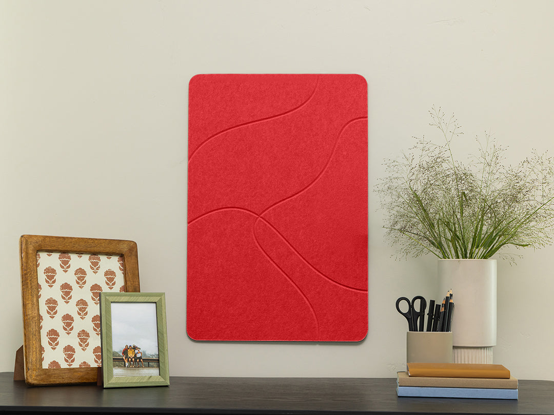 Red decorative wall panel on a white wall with a shelf featuring a picture frame, plant, and stationery items.