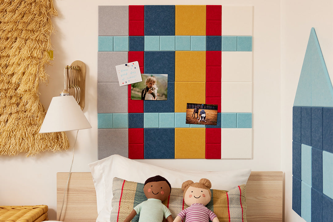 Felt Right plaid design using shades of blues, red, yellow, white, and grey felt square tiles in a kids room above the bed and picutres pinned on the felt tiles