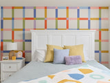 Felt Right wall art design in a bedroom with a plaid design using pink, orange, green, and blue felt tiles behind a bed and a night stand.