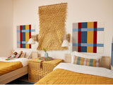 A Felt right wall art design on a white wall in a children's bedroom above two beds using red, blue, and yellow felt tiles.