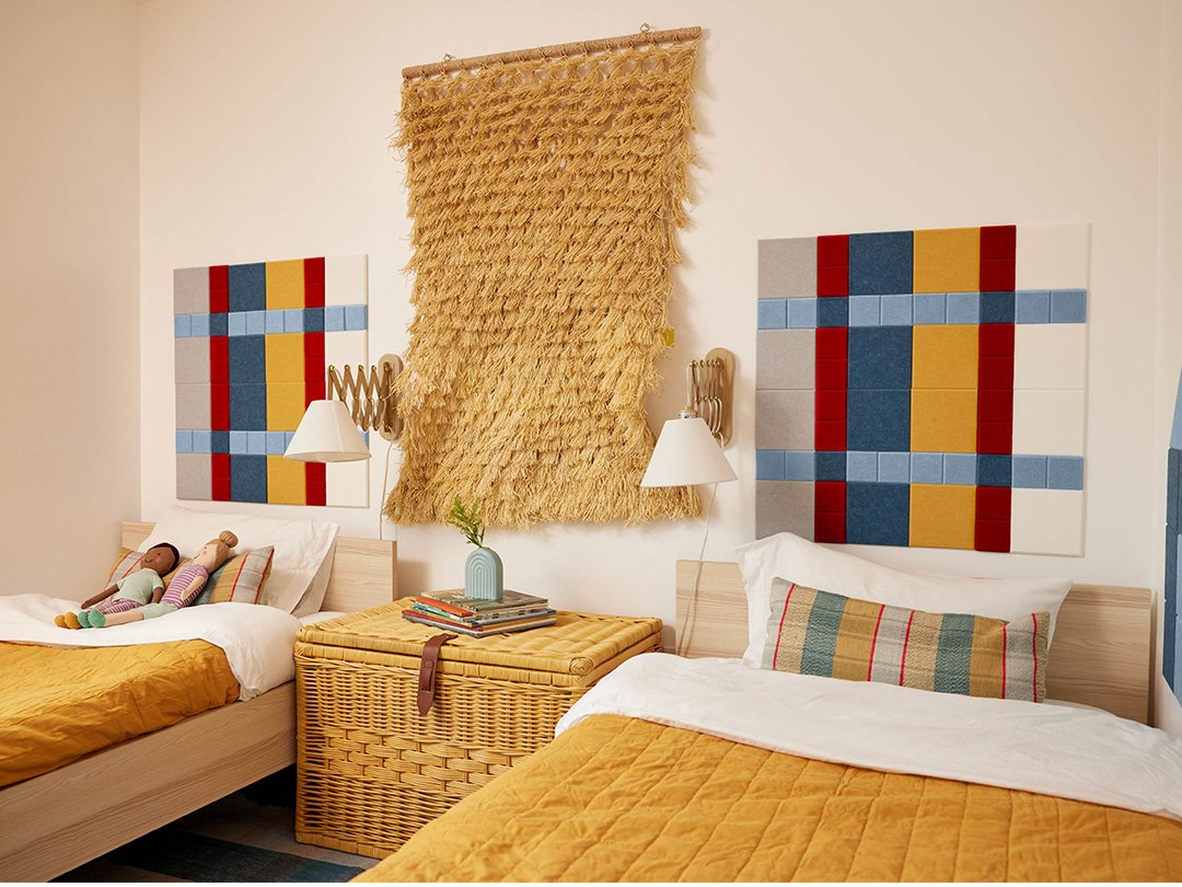 A Felt right wall art design on a white wall in a children's bedroom above two beds using red, blue, and yellow felt tiles.